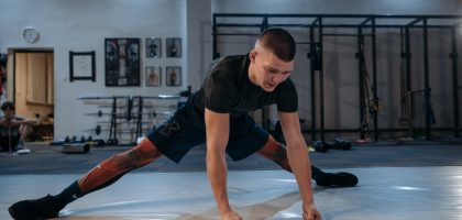 A male athlete stretches intensely in a dimly lit gym environment, preparing for training.
