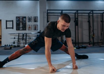 A male athlete stretches intensely in a dimly lit gym environment, preparing for training.