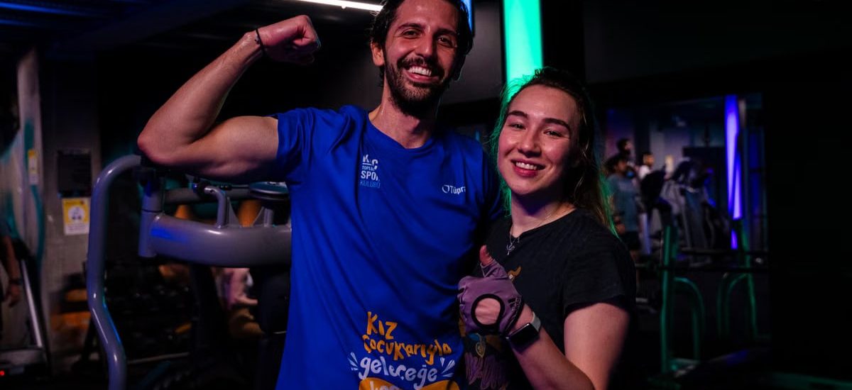 Happy couple in sportswear posing confidently at a gym, showing fitness enthusiasm.