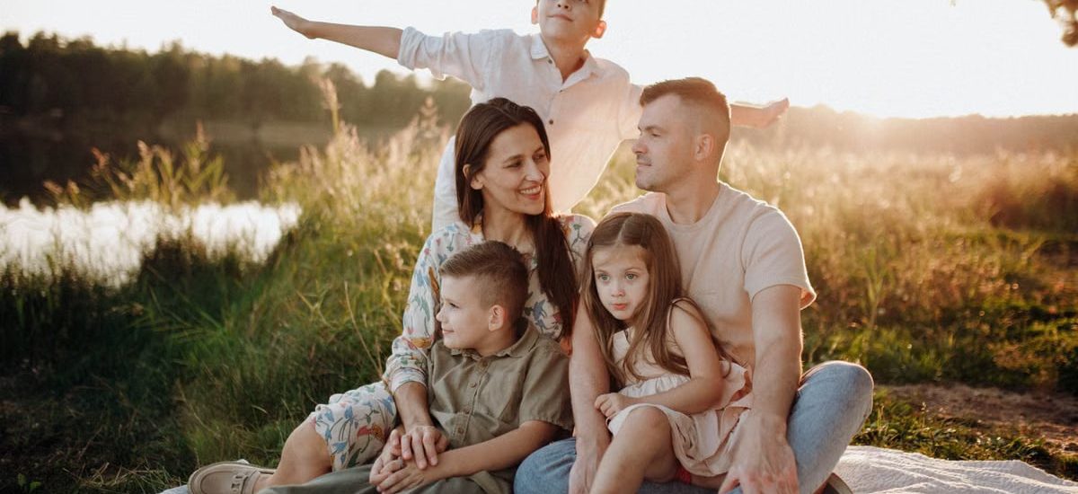 A family of five enjoying a serene picnic in a sunlit meadow during sunset.