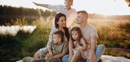 A family of five enjoying a serene picnic in a sunlit meadow during sunset.